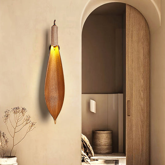 The leaf sconce lit on a plaster wall beside an arched wood doorway