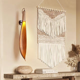 The leaf sconce lit beside a macrame hanging above a stone console with books