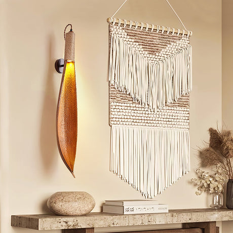 The leaf sconce lit beside a macrame hanging above a stone console with books