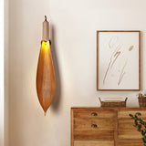 The leaf sconce lit above a wood chest of drawers beside a framed line drawing