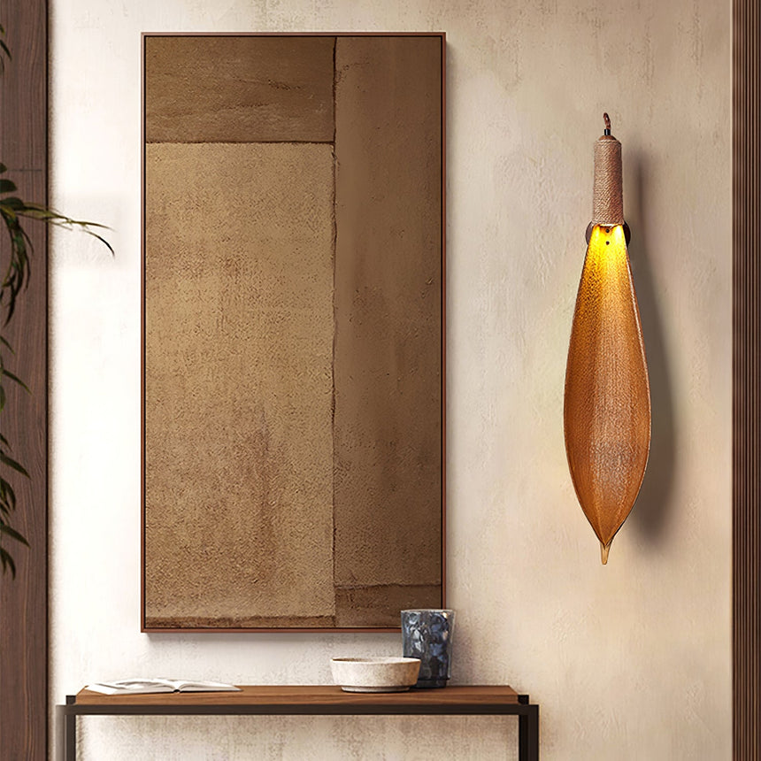 The leaf sconce lit beside a wood panel above a narrow entry table