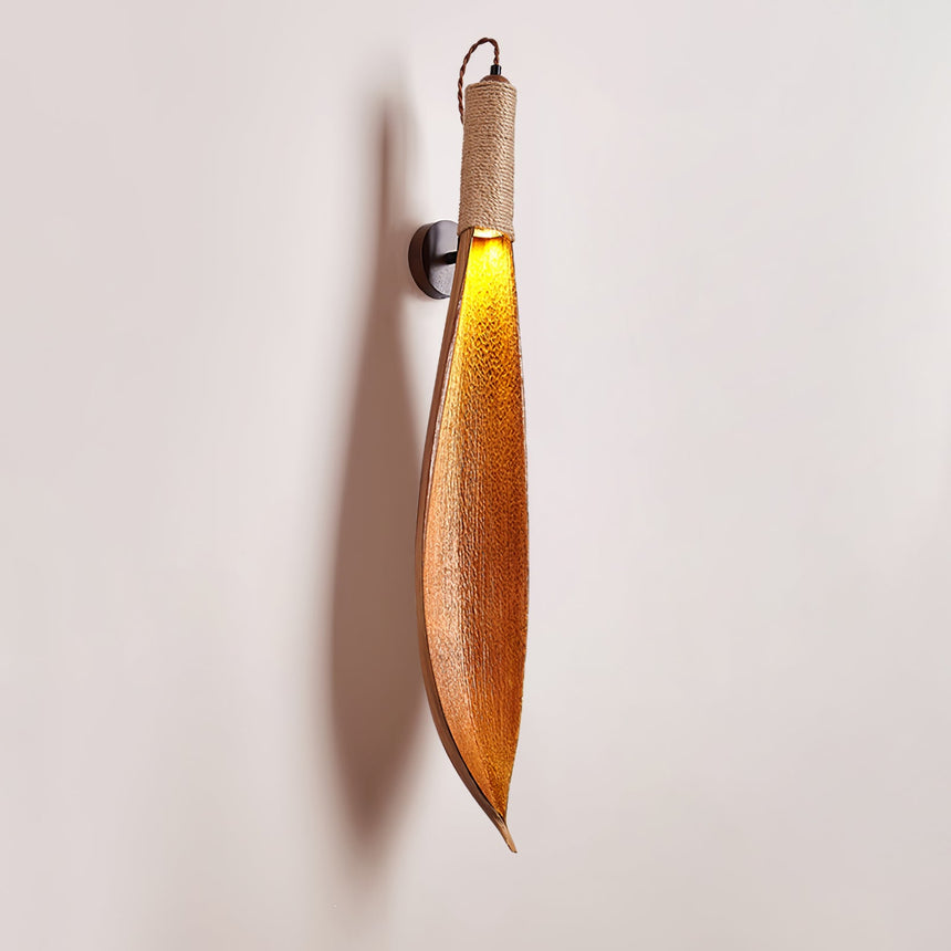 The leaf sconce lit on a plain wall, the black bracket and jute wrap visible