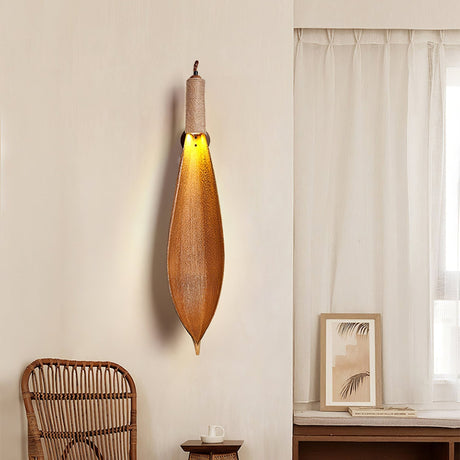 The leaf sconce lit above a rattan chair beside a white curtain