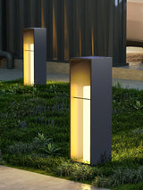 Two lit on grass beside pale paving with a dark timber wall behind