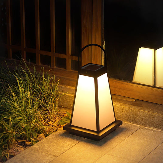 The lantern lit beside ornamental grasses at the edge of a timber deck
