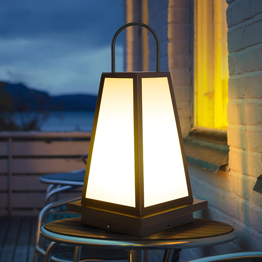 The lantern lit on a round terrace table with the sea behind at dusk