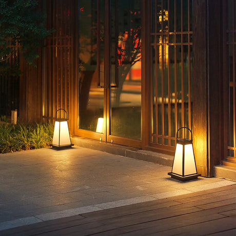 Lanterns lit along a paved path beside a slatted gate and planting