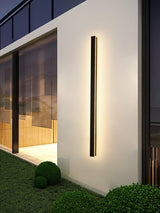 A strip lit on a white wall above a lawn and a round clipped shrub