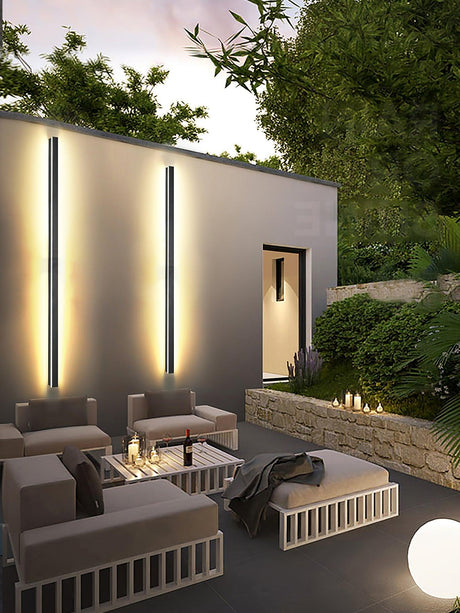 Two tall strips lit on a garden wall above a patio sofa set and a low table