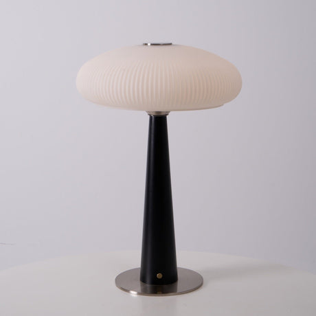 LED table lamp lit in a warm tone on a wooden plinth in a pale room