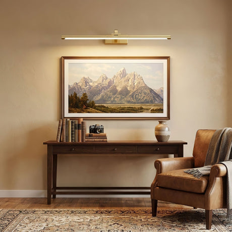 Brass bar lit above a framed landscape over a console with a lamp and a chair