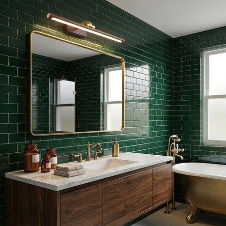 Brass bar lit above a framed mirror on a green tiled wall over a walnut vanity