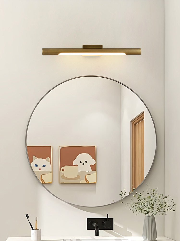 Brass tube above a round mirror over a white basin with framed prints