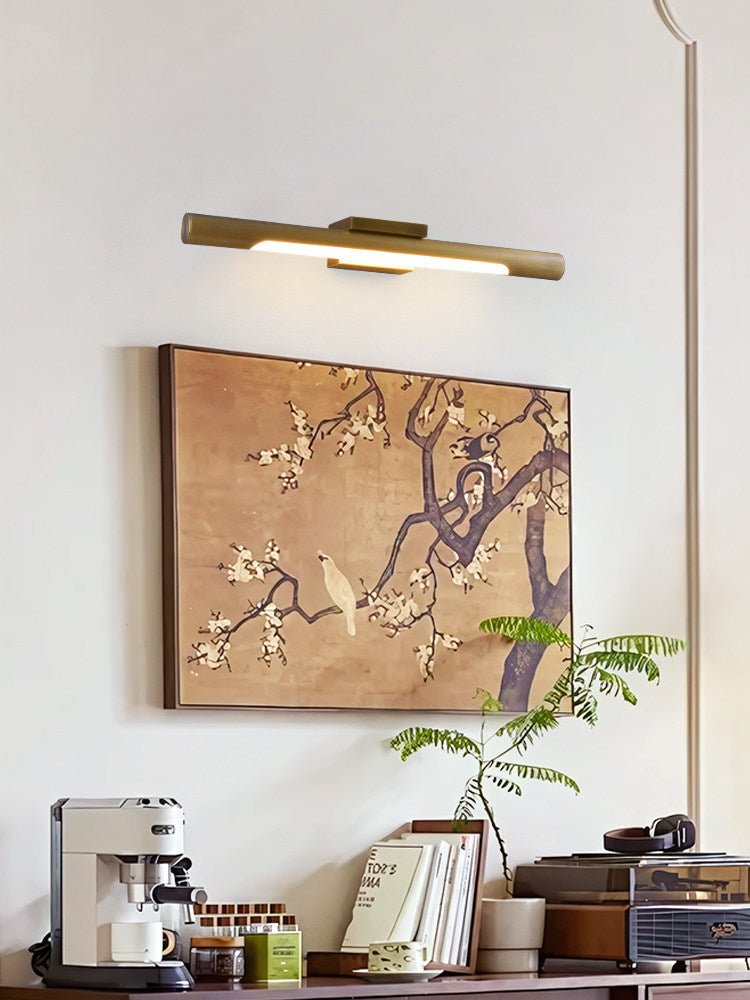 Brass tube lit over a framed painting above a counter with a coffee maker