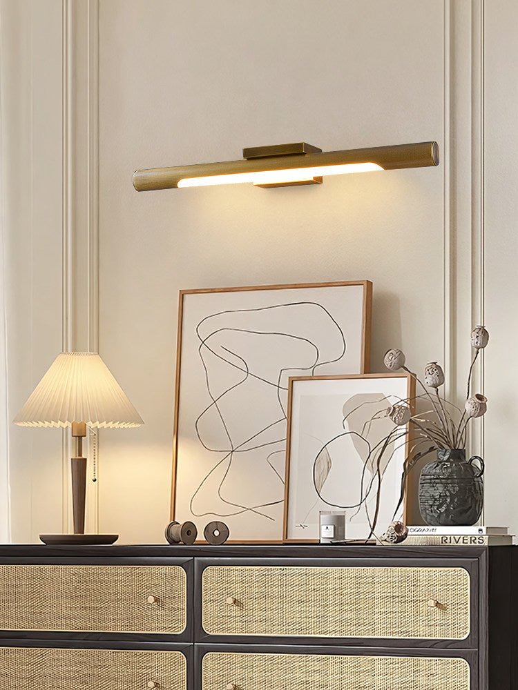 Brass tube lit over framed art above a rattan fronted dresser and a lamp