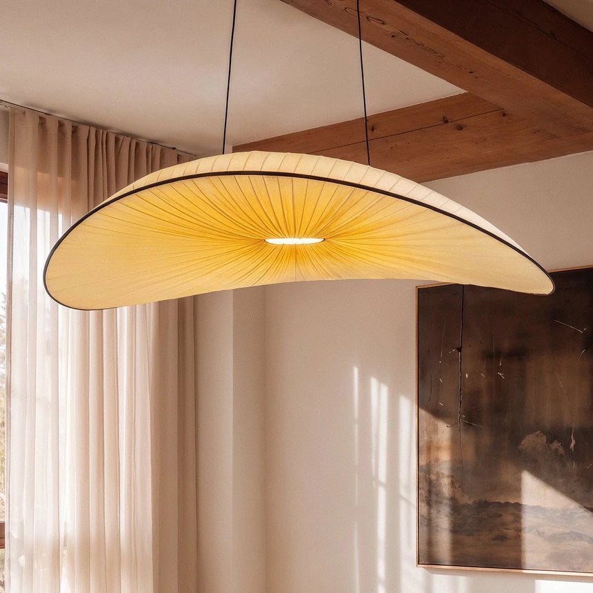 The lit shade beside pale curtains under an exposed wood ceiling beam