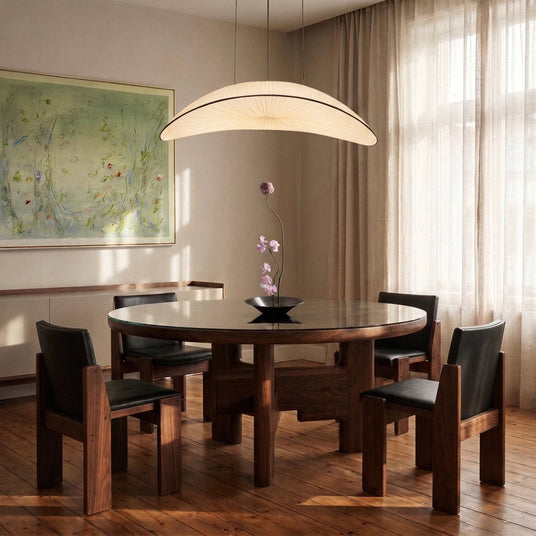 The lit shade above a round wood dining table with four dark chairs and curtains