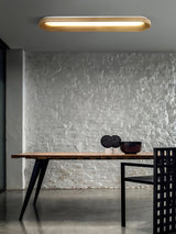 Linear wood frame ceiling light above a dark dining table with a textured wall