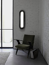 Linear ceiling light on a white brick wall above a dark armchair