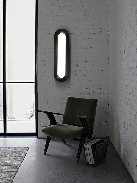Linear ceiling light on a white brick wall above a dark armchair