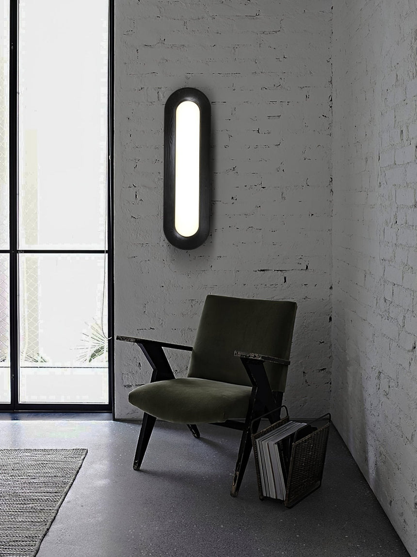 Linear ceiling light on a white brick wall above a dark armchair