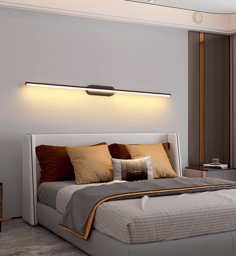 Thin rod lit above a wide bed with a gold trimmed headboard in a gray bedroom