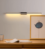 Thin rod lit above a wood desk with an open book and a framed print leaning