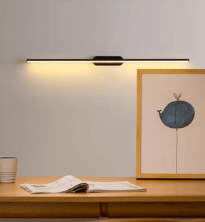 Thin rod lit above a wood desk with an open book and a framed print leaning
