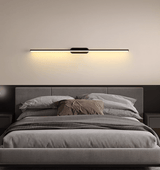 Thin rod lit above a bed with a dark headboard and a striped throw