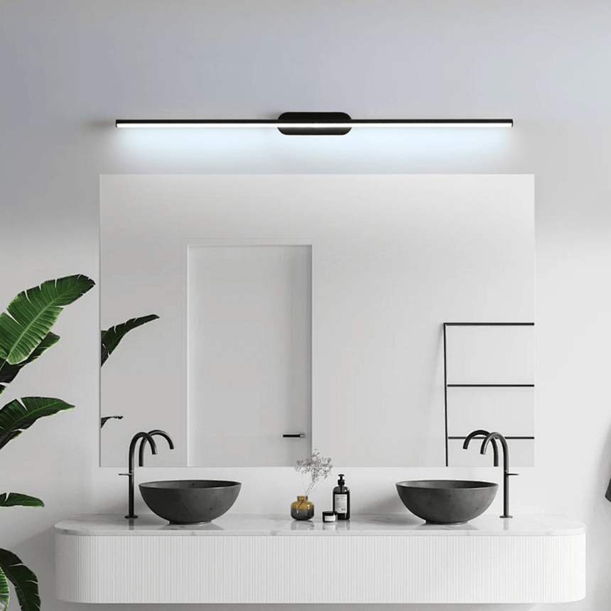 Thin rod lit above a bathroom mirror over two basins beside a large leafy plant