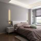Lit beside a bed with a padded headboard, a nightstand and a window behind