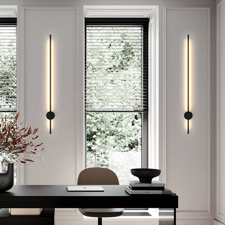 A pair lit either side of a window above a dark desk with a vase and a chair
