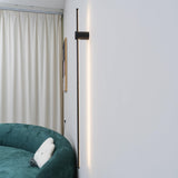 Lit beside a long curtain above a green armchair in a pale corner of a room
