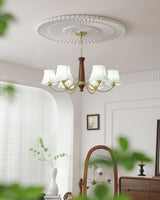 Chandelier lit beside an arched mirror above a sideboard and vase