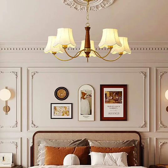 Chandelier lit in a bedroom above a bed with rust colored pillows
