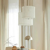 Linen drum pendant light hung in front of a tall curtained window