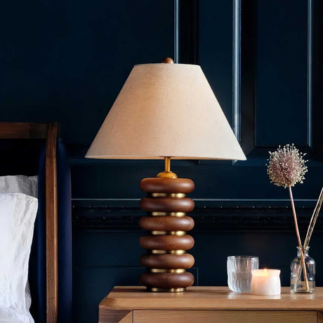 Linen shade table lamp lit on a nightstand against a navy wall