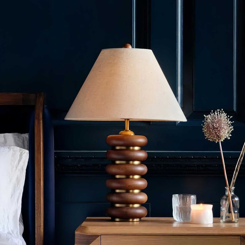 Linen shade table lamp lit on a nightstand against a navy wall