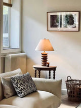 Linen shade table lamp lit on a side table in a reading corner