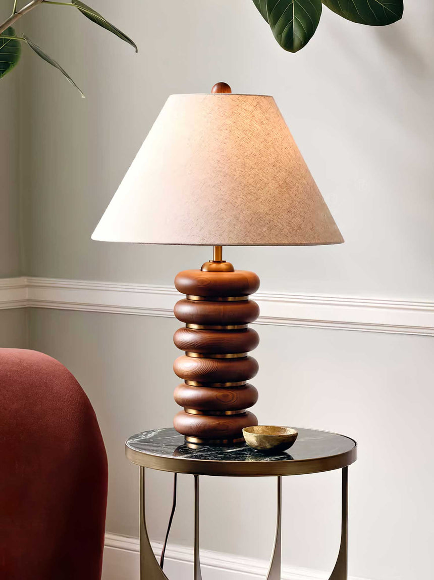 Linen shade table lamp lit on a side table by a red armchair