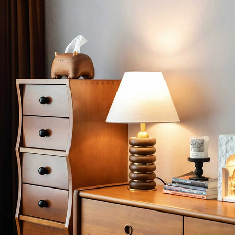 Linen shade table lamp lit on a dresser beside a tissue box