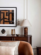 Linen shade table lamp on a sideboard beside a tan cushion