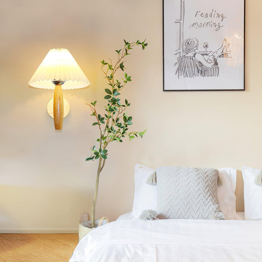 Sconce lit above a bed beside a framed print and a tall trailing plant