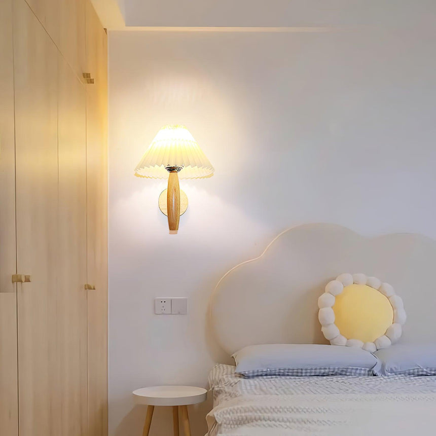 Sconce lit in a bedroom nook above a bed with a round cushion and a stool