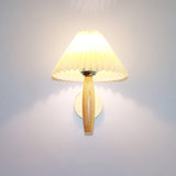 The pleated linen shade lit warm on its oak arm, light spilling up the wall