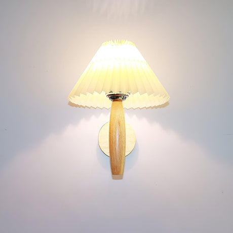 The pleated linen shade lit warm on its oak arm, light spilling up the wall