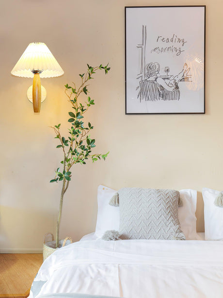 Sconce lit beside a framed print above a bed with white pillows and a plant