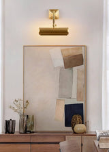 Brass tube lit over a framed artwork above a wood dresser and vases
