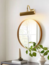 Brass tube above a round mirror with a leafy branch in a pale vase