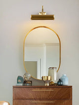 Brass tube lit above a mirror over a walnut dresser with small objects